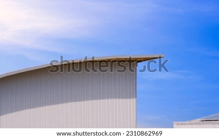 Side view of corrugated iron wall with curve shed roof of modern warehouse building against blue sky background