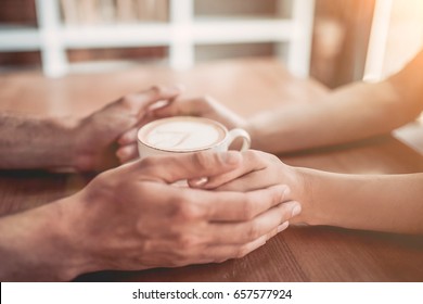 Side View Of Couple In Love Holding Hands With Coffee On Wooden Table.