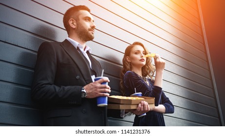 side view of couple in luxury outfit with soda drinks and italian pizza on street