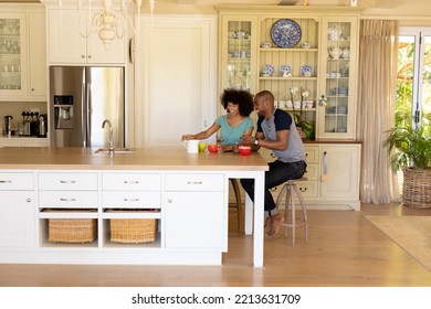 Side View Of A  Couple Sitting At The Kitchen Island With Cups Of Coffee And Talking 