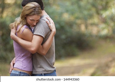 Side View Of A Couple Standing On Forest Trail And Hugging