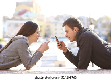 Side view of a couple of teens lying on the floor of a street and obsessed everyone with his smart phone and ignoring each other