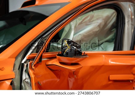 Side view of crashed orange car with deployed airbag.