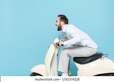 Side view of crazy screaming young bearded man guy in casual light shirt driving moped isolated on pastel blue background studio portrait. Driving motorbike transportation concept. Mock up copy space