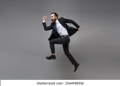 Side view of crazy young business man in classic suit shirt tie posing isolated on grey background. Achievement career wealth business concept. Mock up copy space. Jumping, running, fooling around