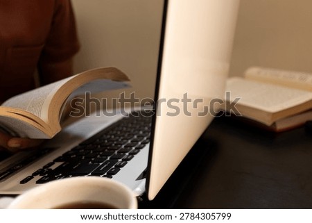 Side view of a creative freelancer flipping pages of a textbook near an open computer and a cup of coffee.