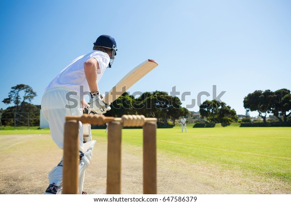 Side view of cricket player batting while playing on\
field against clear sky