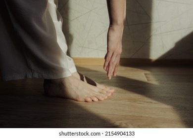 Side view of crop barefoot woman doing forward bend and practicing yoga in Uttanasana while standing in room with sunlight 