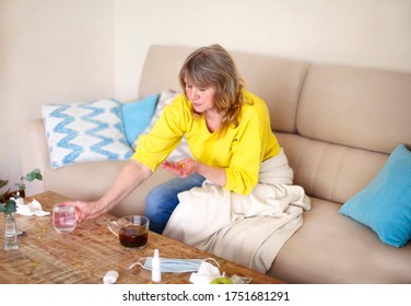 Side View Of Crop Middle Aged Female Taking Pills Bottle While Sitting At Table With Glass Of The Water And Protective Mask At Home