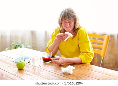 Side View Of Crop Middle Aged Female Taking Pills While Sitting At Table With Cup Of Tea And Protective Mask At Home