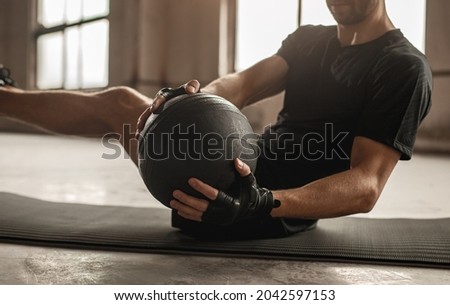 Side view of crop unrecognizable athletic male doing side twist exercise with medicine ball during intense functional training in gym