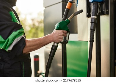 Side view of crop unrecognizable male in uniform inserting fuel nozzle into dispenser after filling vehicle during work at gas station - Shutterstock ID 2179679555