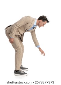 side view of curious smart casual man leaning forward  and reaching his hand to grab something from the ground