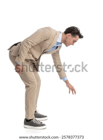 side view of curious smart casual man leaning forward  and reaching his hand to grab something from the ground