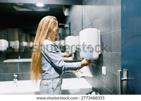 Side view of customer taking paper towel to dry hands in modern shopping mall restroom.