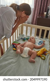 Side View Cute Baby Without Clothes Lying Naked In Crib Looking At Active Mother Hiding And Showing Her Face, Playing Peek-a-boo. Mother Entartaining Baby In Bed.