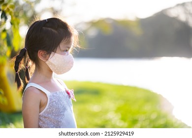 Side View Of Cute Kid Girl Wearing Cloth Face Mask Was Standing In Park In Evening. During Summer Or Spring. Relax Time. Empty Space To Enter Text. Child Age 5 Years Old.