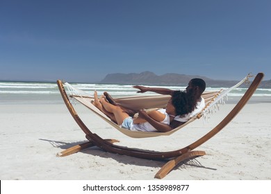 Side view of cute multi-ethnic couple relaxing on hammock while African American male points at something in front of them at beach on sunny day - Powered by Shutterstock