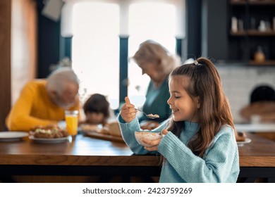 Side view of cute small girl holding bowl with cereals and smiling at grandparent's home. - Powered by Shutterstock