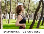 Side view of cute sportive woman wearing black sports bra standing on city park, outdoors enjoying stress free mindful moment, doing yoga relaxation exercises, closed eyes, meditating nature.