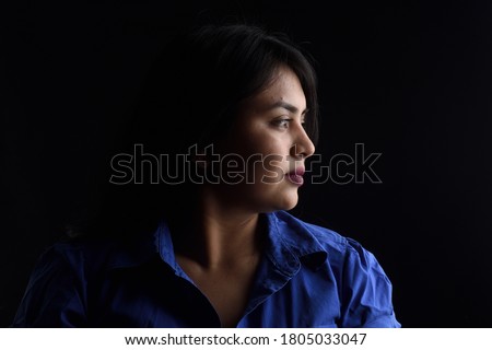 side view of dark portrait of a latin woman on black background, serious