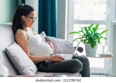 Side view dark-haired pregnant woman in glasses sit on comfortable grey couch having computer on knees and working as freelancer at home in pleasant interior. Remote work, overwork  - Powered by Shutterstock