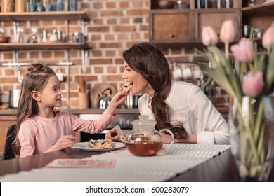 'side view of daughter feeding mother with cake on mother's day holiday in kitchen - Powered by Shutterstock