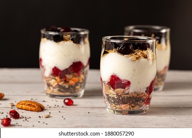 Side view of Delicious fruit and yogurt parfait  cups filled with layers of muesli, chia seeds, fresh berries, rolled oats, and homemade yogurt served with pomegranate and pecan on wooden background. - Powered by Shutterstock