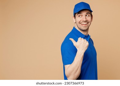 Side view delivery guy employee man wearing blue cap t-shirt uniform workwear work as dealer courier point thumb finger aside indicate on area isolated on plain light beige background. Service concept - Powered by Shutterstock