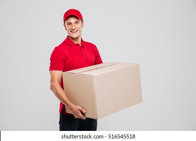 Side View Of Delivery Man With Box In Studio. Isolated Gray Background