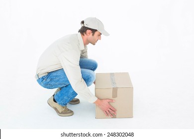 Side View Of Delivery Man Crouching While Picking Cardboard Box Against White Background