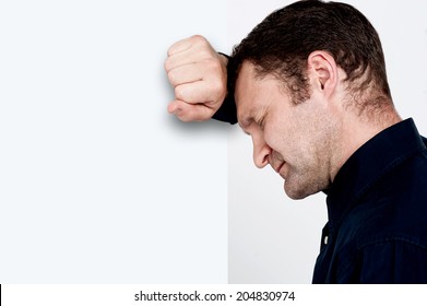 Side view of depressed man leaning his head against a wall