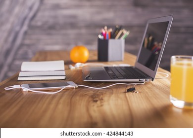 Side View Of Designer Desktop With Laptop, Smartphone, Office Tools And Orange. Angled Laptop On Table In Home Interior. Freelance Desktop With Open Laptop Computer