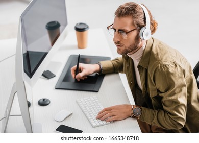 Side view of digital designer in headphones using graphics tablet and computers while working in office - Powered by Shutterstock