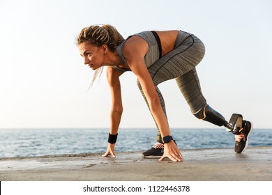 Side View Of Disabled Athlete Woman With Prosthetic Leg Starting To Run Outdoor At The Beach