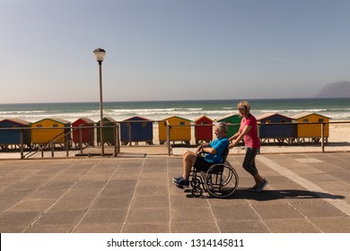 Side view of disabled senior man being pushed on wheelchair by senior woman at beach on a sunny day - Powered by Shutterstock