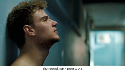 Side view of disappointed and tired sportsman wiping face and leaning on wall in semilit locker room. - Powered by Shutterstock