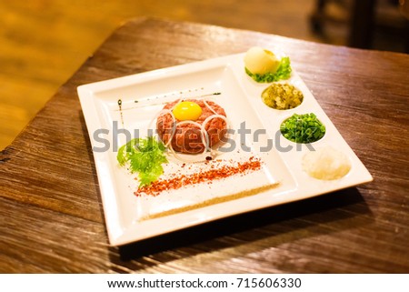 The side view of the dish consisted of the raw meat, egg yolk, lettuce, spices, greens and onions.