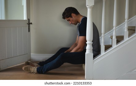 Side View Of A Distressed Caucasian Man At Home, Sitting On The Stairs Looking Down. Home And Lifestyle Weekend Activities.