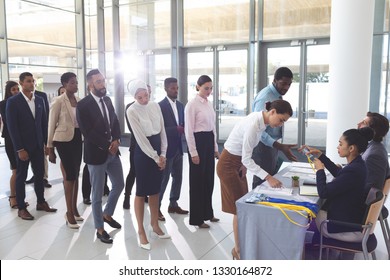 Side view of diverse business people checking in at conference registration table while mixed-race businesswoman wearing hijab looks at table in office lobby