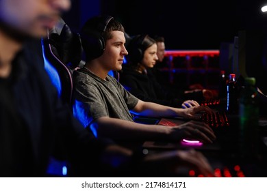 Side View At Diverse Cyber Sport Team Playing Video Games In Row, Focus On Caucasian Young Man Wearing Headphones