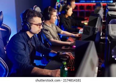 Side View At Diverse Cyber Sport Team Playing Video Games In Row, Focus On Middle Eastern Young Man In Foreground