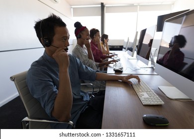 Side view of diverse executives talking on headset while looking at computer screens in modern office