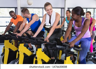 Side View Of Diverse Fit People Exercising On Exercise Bike In Fitness Center. Bright Modern Gym With Fit Healthy People Working Out And Training At Spin Class