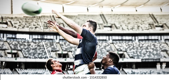 Side view of diverse male rugby players trying to catch the ball in the air while team members hold them in the air in stadium on sunny day. - Powered by Shutterstock