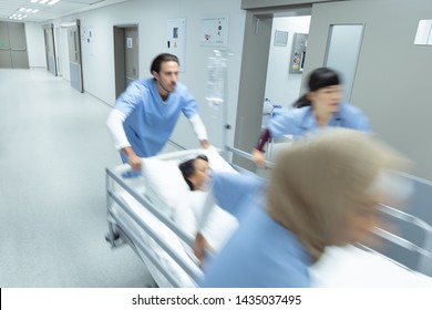 Side View Of Diverse Medical Team Pushing Emergency Stretcher Bed In Corridor At Hospital