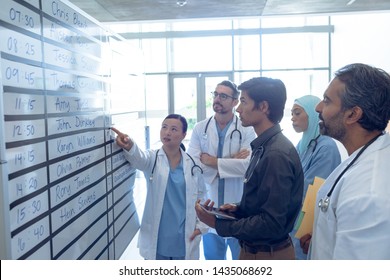 Side view of diverse medical team of doctors discussing their shifts on chart at hospital. Asian female surgeon is pointing at the whiteboard. - Powered by Shutterstock