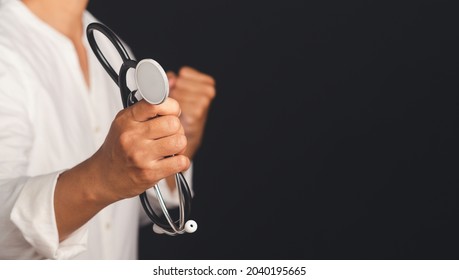 Side View Of A Doctor Holding A Stethoscope And Fist Symbol Fight Various Diseases While Standing On Black Background. Space For Text. Medical And Healthcare Concept.