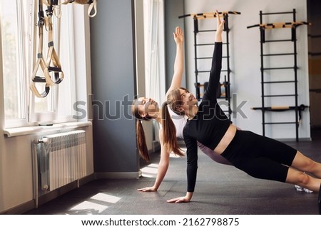 Side view. Doing stretches. Two women in sportive clothes have fitness day in the gym together.