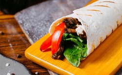 Side View Of Doner Kebab Wrapped In Lavash On Wooden Board